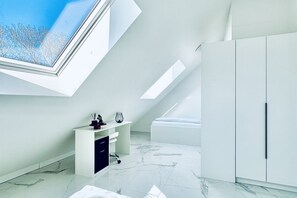 A modern, minimalist room with a skylight, a white desk, a bed, and a wardrobe.