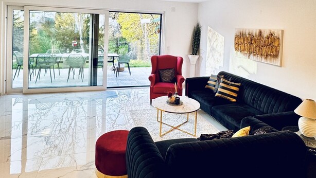 A living room with a black sofa, red armchair, and a glass door leading to an outdoor patio. - Quiet Luxury 5BR & 1LR Villa w/ Garden & Terrace (Mödling)