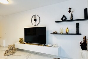 Ein modernes Wohnzimmer mit Flachbildfernseher, weißen Schränken, Dekorationselementen auf Regalen und einem Marmorboden.