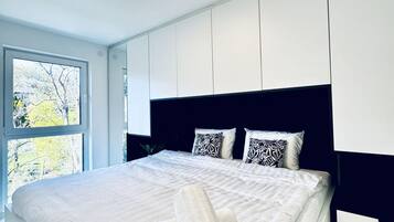 Un dormitorio moderno con una cama grande, paredes blancas y un ventanal con vistas a árboles.