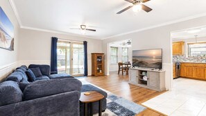 Een woonkamer met een bank, televisie en kasten, een eethoek met stoelen, en een keuken met houten kasten.