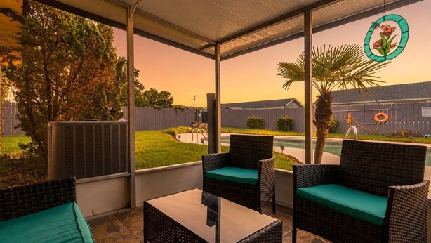 A covered patio with wicker furniture and a view of a swimming pool and greenery. - Lynn Haven 3BR - Private Pool & Fenced Yard (Lynn Haven)