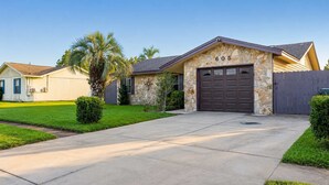 A single-story house with a stone facade, a garage, and a well-maintained lawn. - Lynn Haven 3BR - Private Pool & Fenced Yard (Lynn Haven)