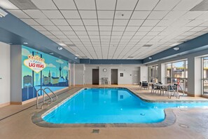 An indoor pool with a cityscape mural, a clock, and a seating area with tables and chairs. - Vegas Condo - Pool, Hot Tub & Balcony Views (Las Vegas)