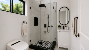 A modern bathroom with a glass-enclosed shower, a toilet, a sink with a mirror, and a window with a view of greenery. - Brand-New Luxury Private ADU, 2BR/2BA, Full Kitchen & Laundry (Fountain Valley)