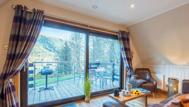 A modern living room with a large sliding glass door leading to a deck with outdoor furniture.