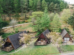Tres cabañas con techos inclinados, rodeadas de un bosque denso. Cada cabaña tiene una terraza y una zona de estar al aire libre.