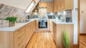 A modern kitchen with wooden cabinets, a built-in oven, a microwave, and a coffee machine.