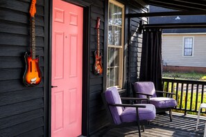 Eine Veranda mit zwei violetten Stühlen, einer roten Tür und zwei Gitarren, die an der Wand lehnen.