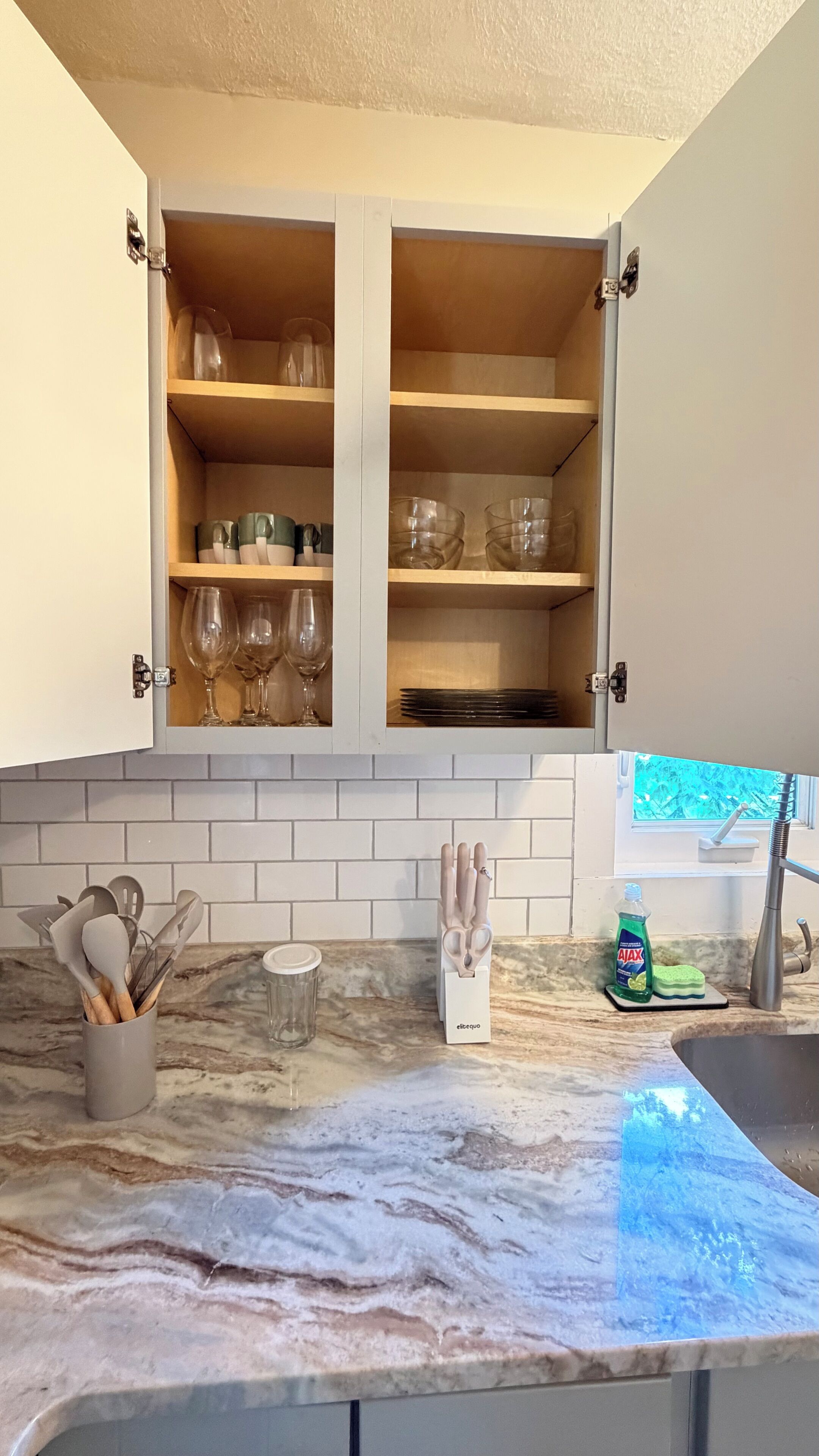 A kitchen with a marble countertop, a cabinet with glassware, and a sink.