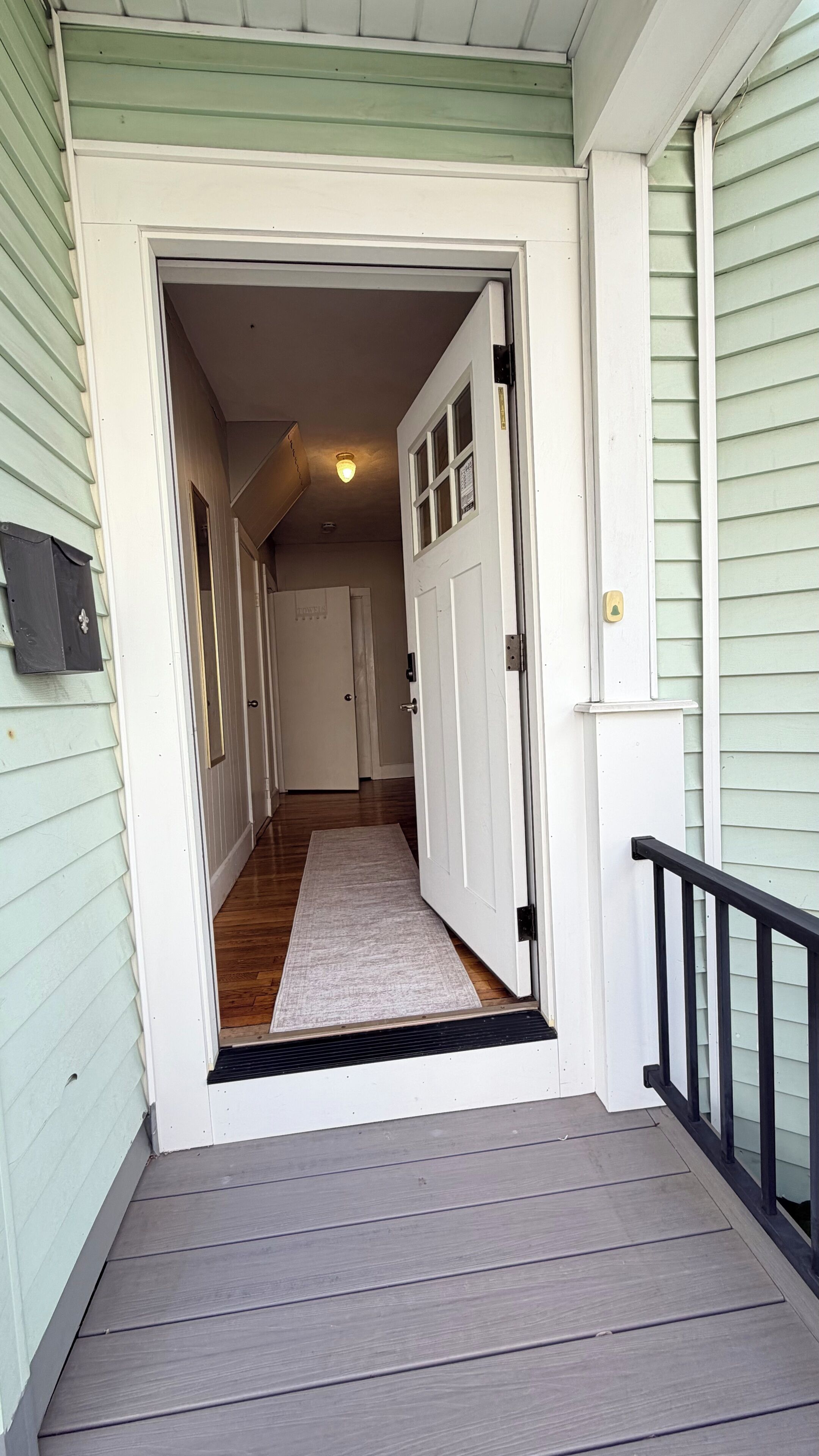 A house entrance with a wooden porch, a door leading to a hallway, and a small rug on the floor.