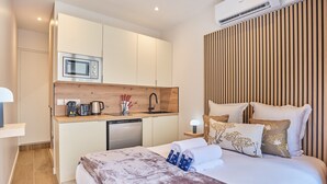 A compact hotel room with a kitchenette, a bed with a duvet and pillows, and a wooden slatted wall. - Charming Suite With AC - Eiffel Tower-beaugrenelle (Paris)