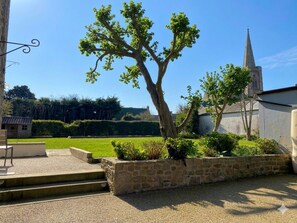 A stone wall with a tree, a chair, and a building with a tower. - Le Nid de Reville, a House Near the See and Shops (Réville)