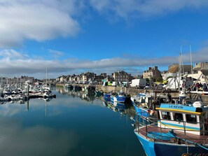 A harbor with boats docked, a white van, and buildings in the background. - Le Nid de Reville, a House Near the See and Shops (Réville)