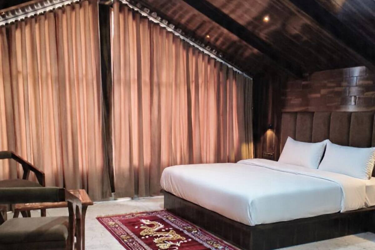 A bedroom with a bed, a chair, a table, and a red patterned rug.