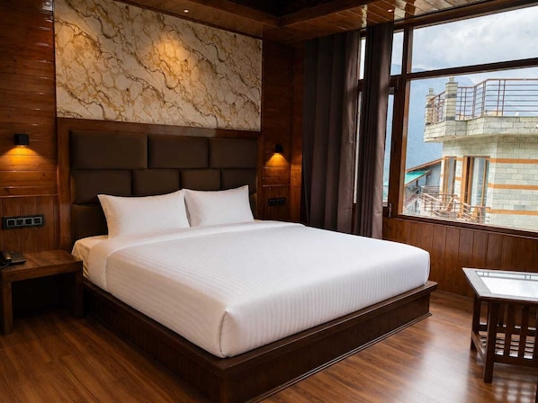 Une chambre d’hôtel avec un grand lit, des boiseries, un mur en marbre et une vue sur les immeubles par la fenêtre.