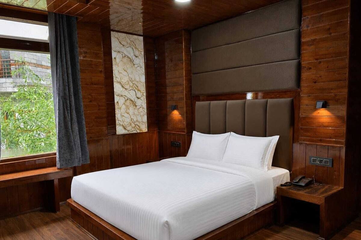 A modern bedroom with a wooden floor, a large bed with white linens, a marble wall, and a window with a view of greenery.