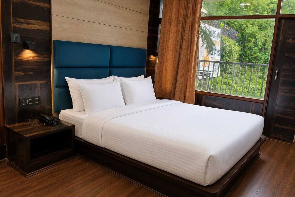 A modern bedroom with a large bed, wooden headboard, and a view of greenery through a window.