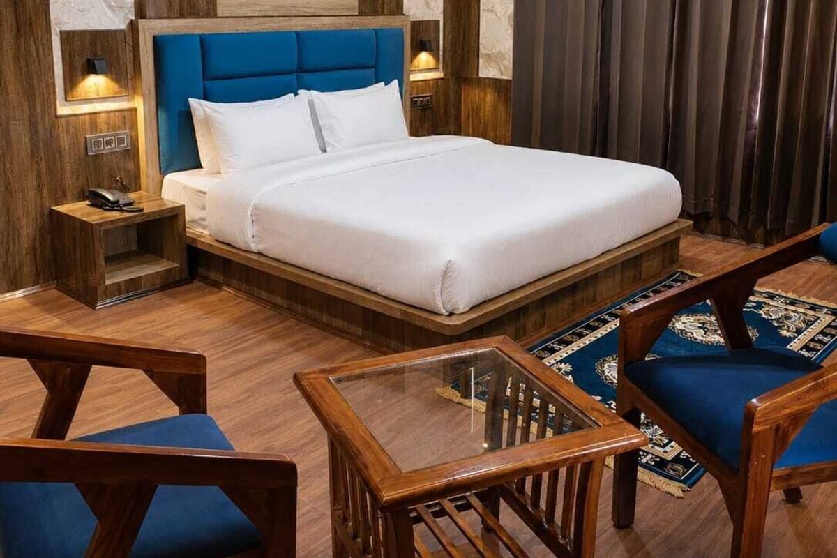 A hotel room with a large bed, wooden headboard, bedside tables, and blue upholstered chairs.