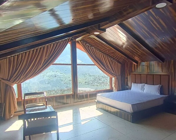 A bedroom with a large window, a bed, a chair, and a small table.