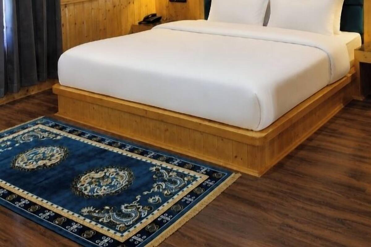 A hotel room with a wooden ceiling, a marble-patterned wall, a bed with white bedding, a nightstand, and a blue patterned rug.