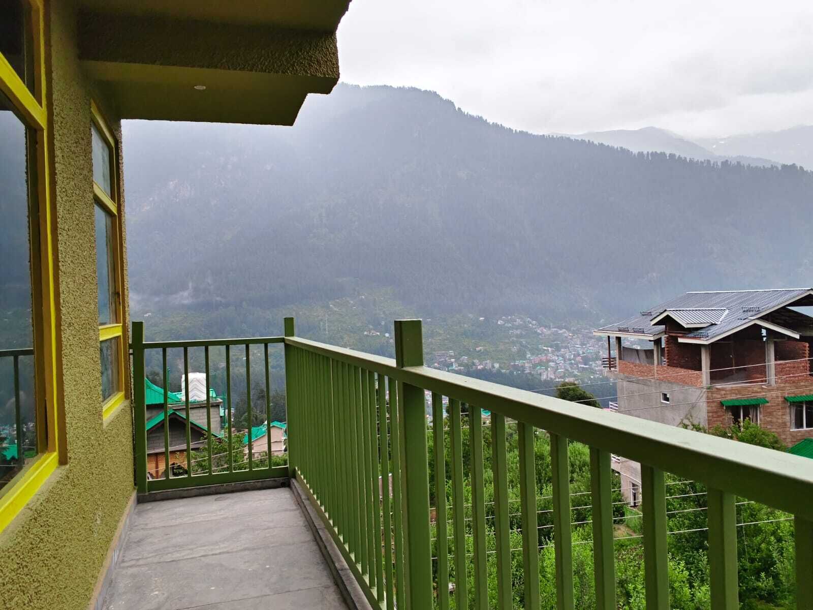 A balcony with a green railing overlooking a mountainous landscape.