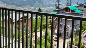 Un balcón con vistas a un paisaje montañoso, un pueblo en la falda de la montaña y un edificio con techo verde.