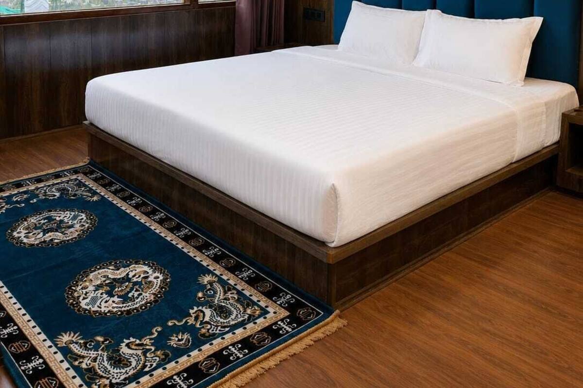 A hotel room with a large bed, a view of a mountainous landscape, a blue patterned rug, and a wooden ceiling.