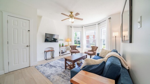 Ein Wohnzimmer mit einer Couch, einem Couchtisch, Stühlen, einem Deckenventilator und einem Fernseher.
