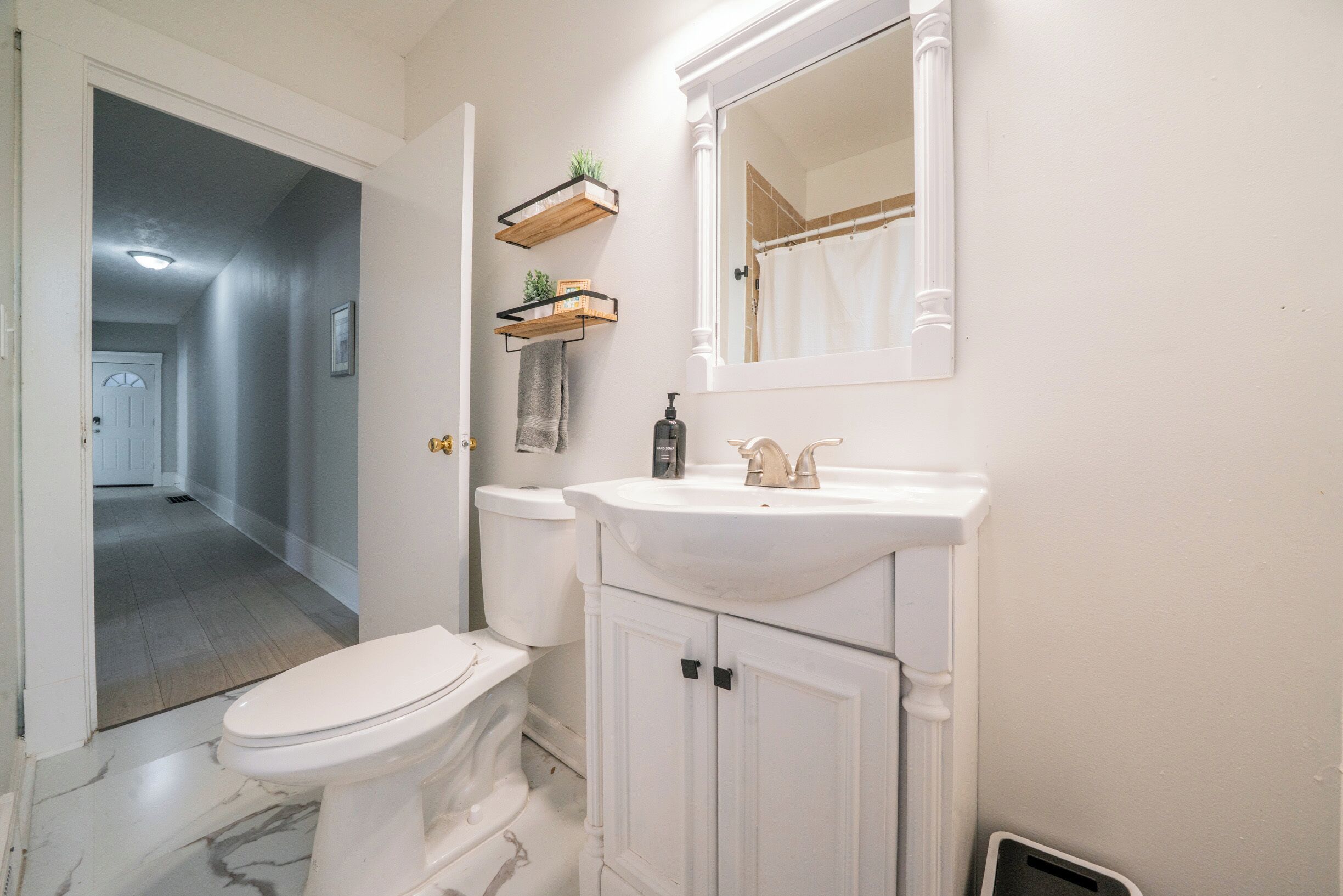 A bathroom with a toilet, sink, mirror, and wooden shelves with plants.