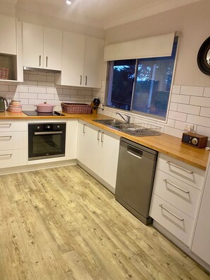 A modern kitchen with white cabinets, a wooden countertop, a dishwasher, an oven, and a window with a view of trees. - “Southerly Change”.
Groovy retro/modern Beach House.
Bring your surfboard & dog! (Moruya Heads)