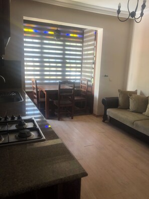 A kitchen with a stove, dining table with chairs, a sofa, and a door leading to a room with striped blinds. - Moonlight terrace  (Fethyie)