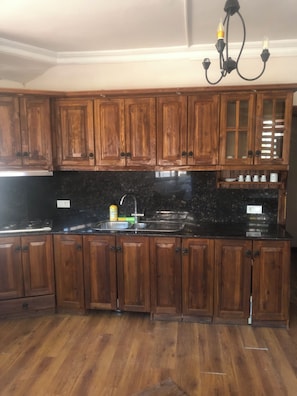 A kitchen with wooden cabinets, a black countertop, a sink, and a chandelier. - Moonlight terrace  (Fethyie)