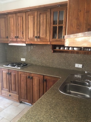 A kitchen with wooden cabinets, granite countertops, a stainless steel sink, and a gas stove. - Moonlight terrace  (Fethyie)