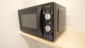 A black microwave on a wooden shelf with power settings and a label indicating 700W. - Toei Stays (Nipponbashi Higashi, Naniwa-ku osaka)