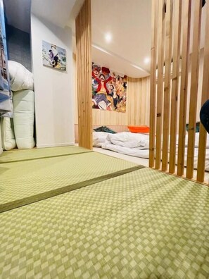 Ein traditioneller japanischer Raum mit Tatami-Matten, einem Futon-Bett, hölzernen Schiebetüren und einem farbenfrohen Wandbild.