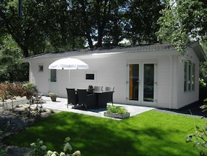 Ein kleines weißes Gebäude mit einer Terrasse, Gartenmöbeln und einem weißen Sonnenschirm.