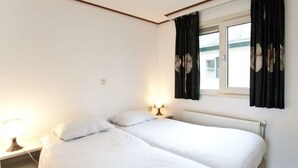 Ett rum med två sängar, ett fönster med gardiner, en sänglampa och ett element.