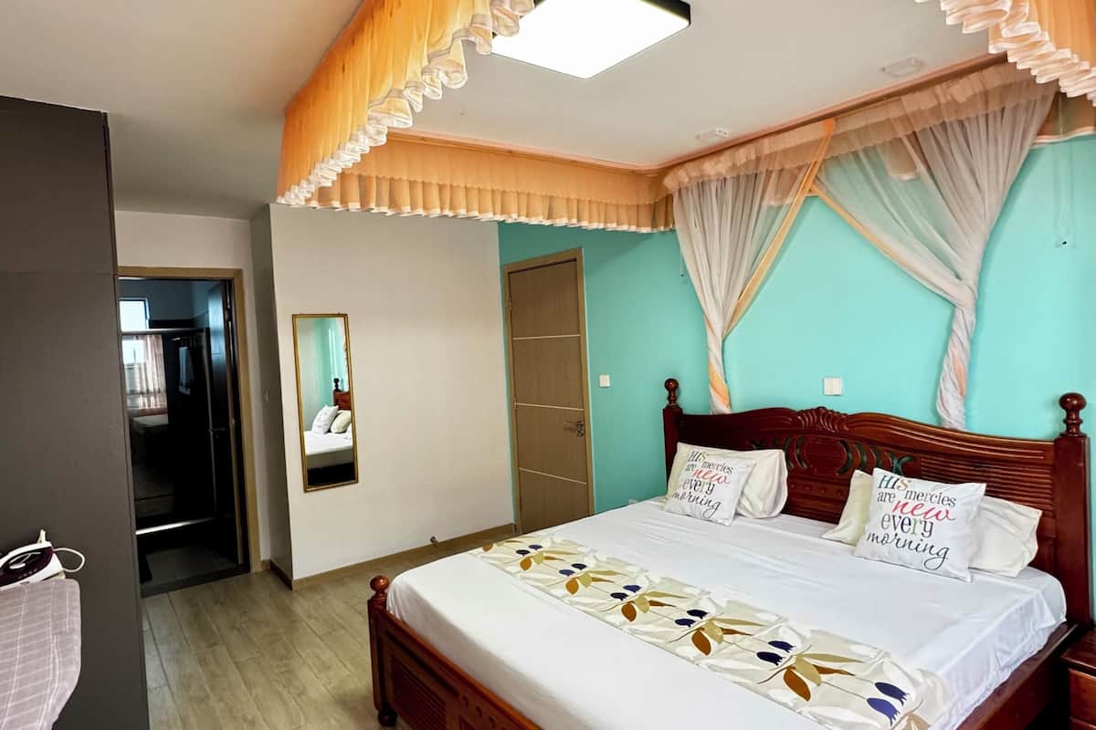 A bedroom with a wooden bed, a mirror, a wardrobe, and a door leading to another room.