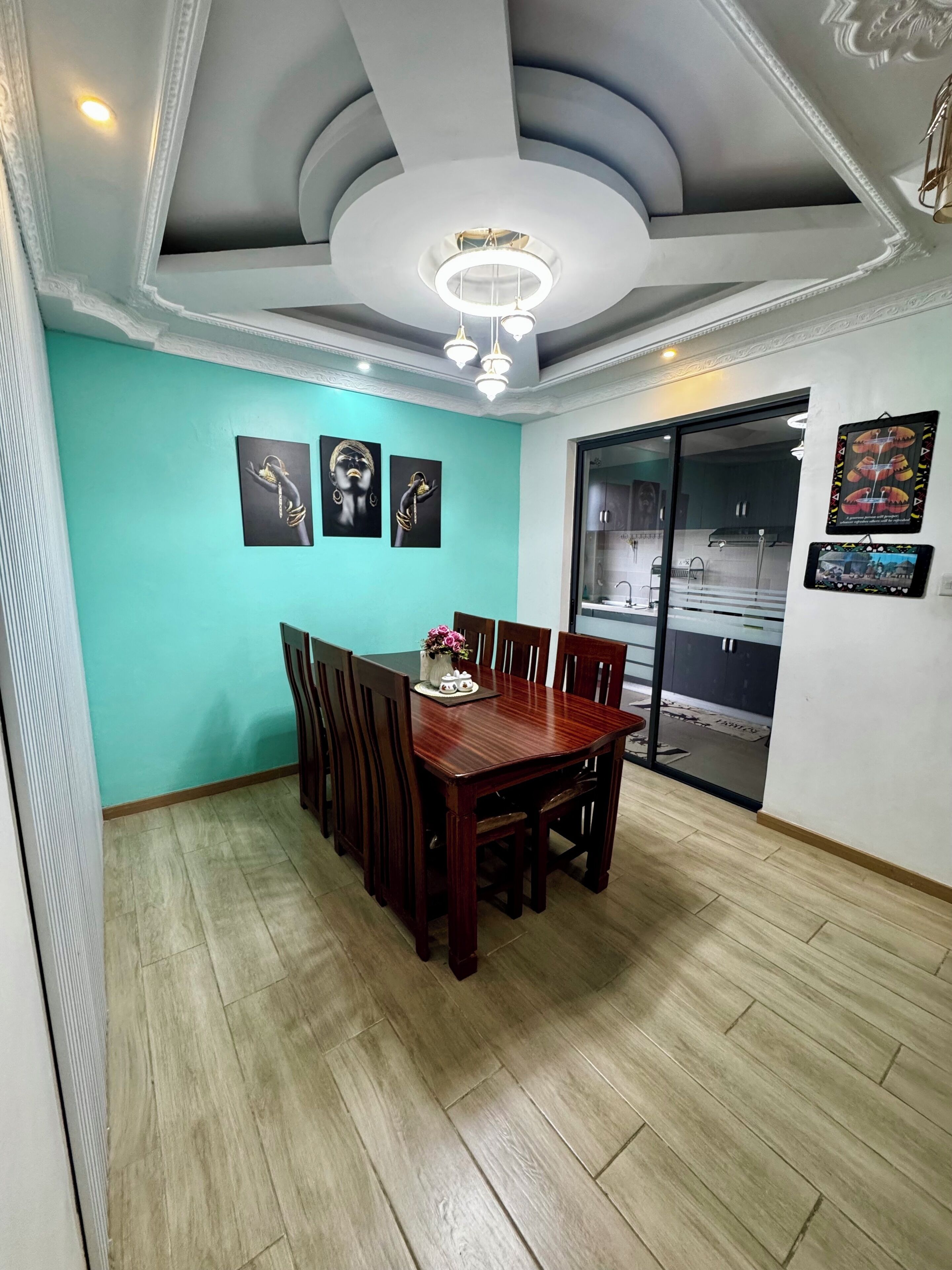 A dining area with a wooden table and chairs, a ceiling light, and wall art.