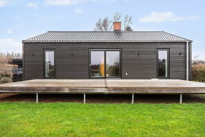 Ein modernes, zweistöckiges Haus mit Flachdach, großen Schiebeglasfenstern und einer Holzterrasse.