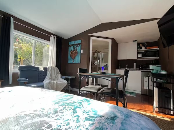 A bedroom with a large bed, a dining area, and a kitchenette.
