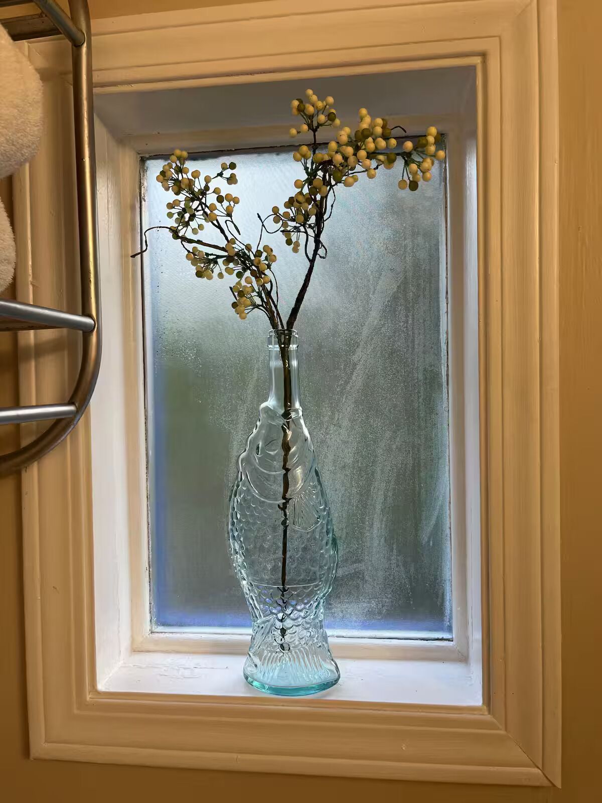En gennemsigtig glasvase med grene og små blade på et vindueskar