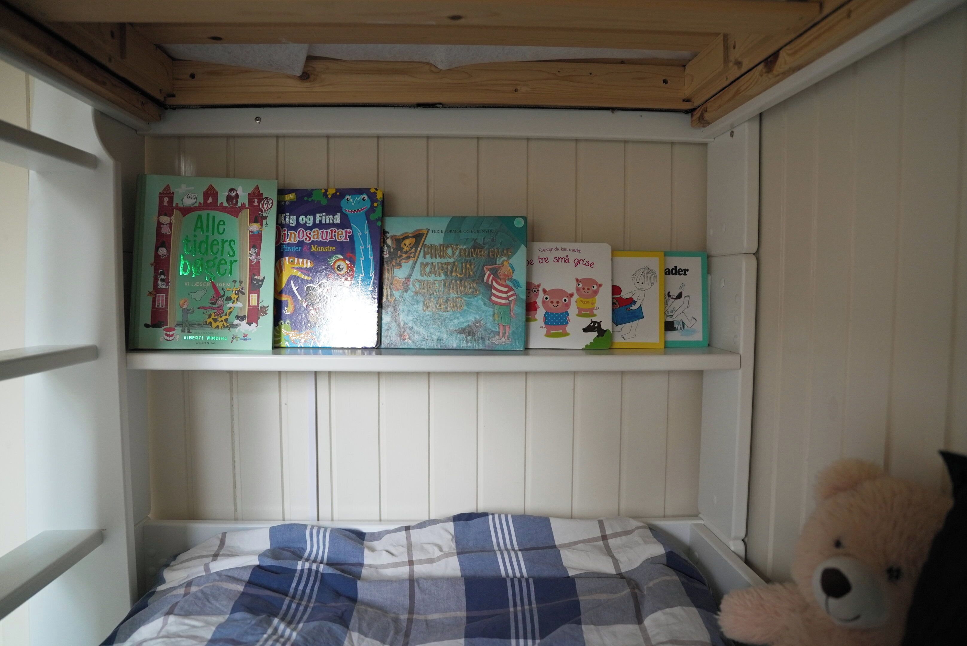 Una habitación infantil con una cama, una estantería con libros y un osito de peluche.
