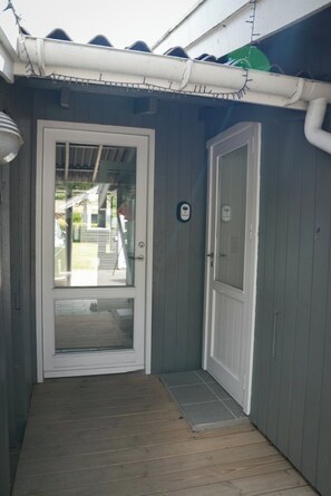 Een houten deur met een ruit, een wit deurkozijn, en een klein portaal met een houten vloer.