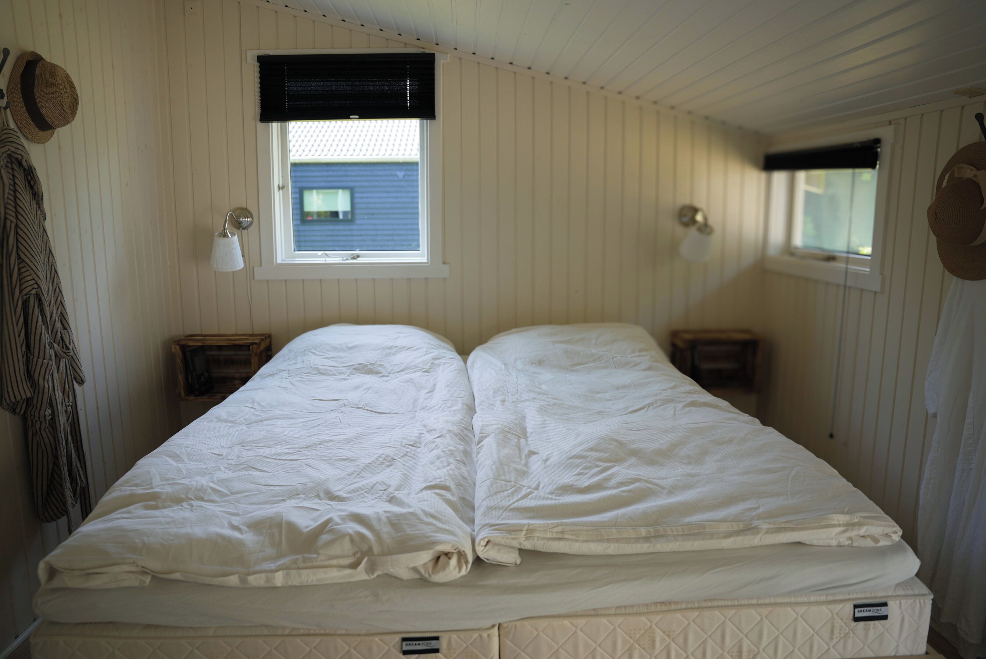 Una habitación con cama, dos mesitas de noche, una ventana con persianas y una lámpara de pared.