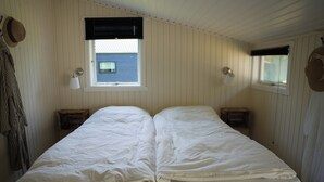 Ein Zimmer mit einem Bett, zwei Nachttischen, einem Fenster mit Jalousien und einer Wandlampe.