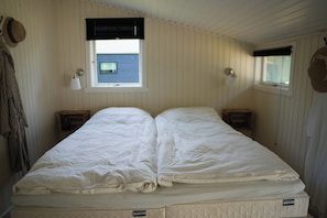 Ein Zimmer mit einem Bett, zwei Nachttischen, einem Fenster mit Jalousien und einer Wandlampe.