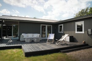 A modern house with a deck, a sofa, two lounge chairs, and a small table. - Family-Friendly Holiday Home with Wilderness Spa (Væggerløse)