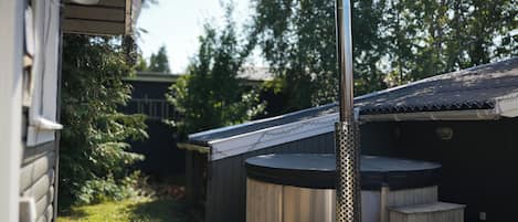 Een sauna met schoorsteen die rook uitstoot, omgeven door houten constructies en een tuin.